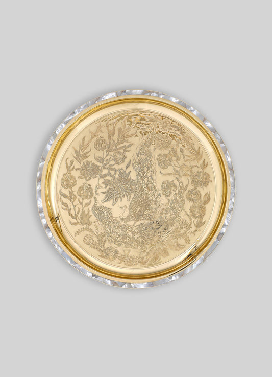 A round decorative tray made of gold-toned metal with intricate engraved floral and peacock motifs, bordered by a clear, faceted acrylic edge.