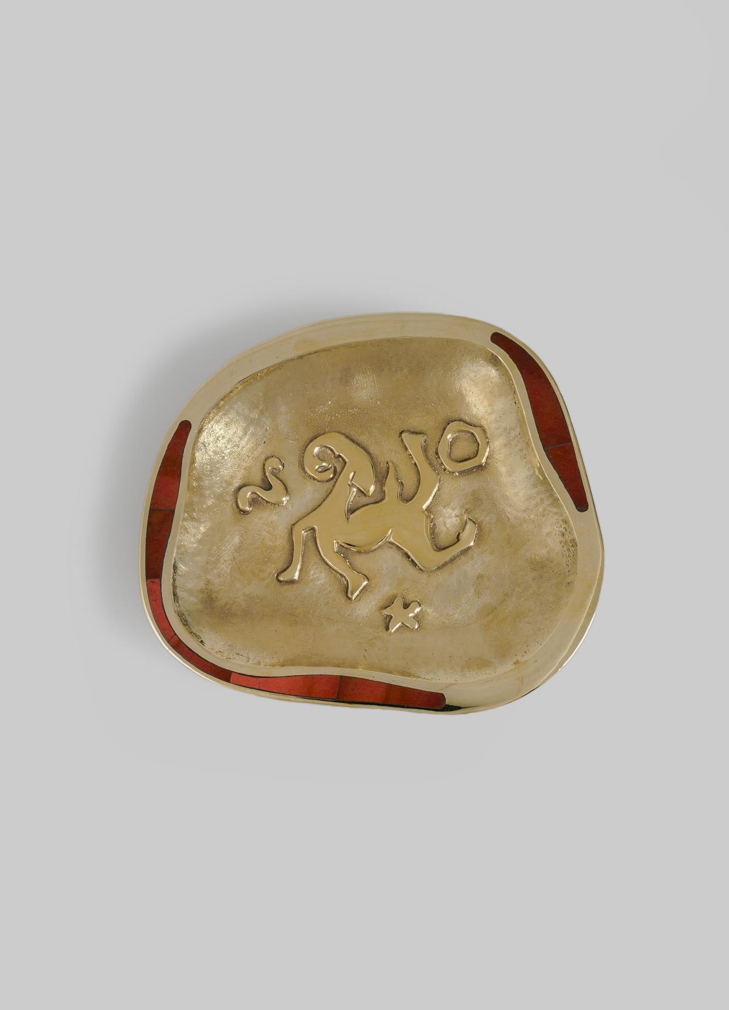 A decorative metal dish with a gold finish features a lion motif and a small star, edged with red accents on two sides.