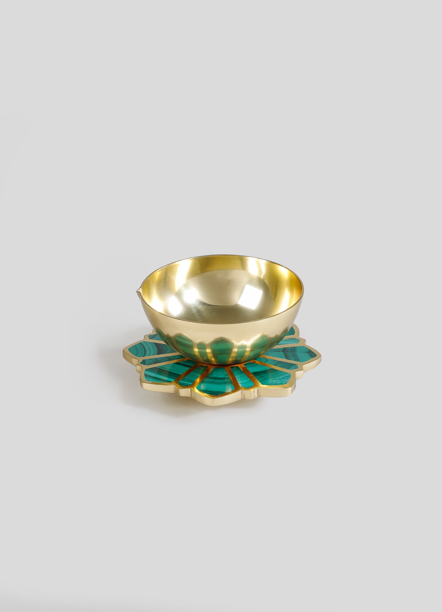 A metallic gold bowl with a reflective finish resting on a decorative tray with a floral motif, featuring green and gold tones. The tray has a scalloped edge and appears to be made of inlay or mosaic materials.