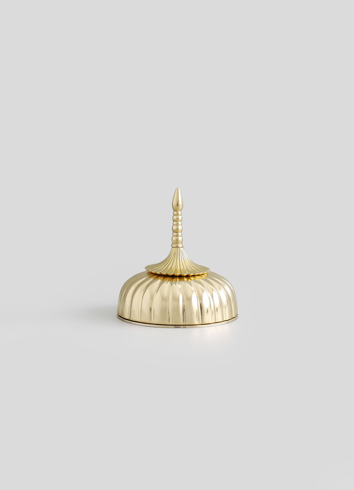 A decorative object resembling a brass or gold-toned container with a scalloped, dome-shaped body, a fluted finial, and a pointed top. The surface features a polished, reflective finish with intricate detailing, giving it an elegant and vintage style.