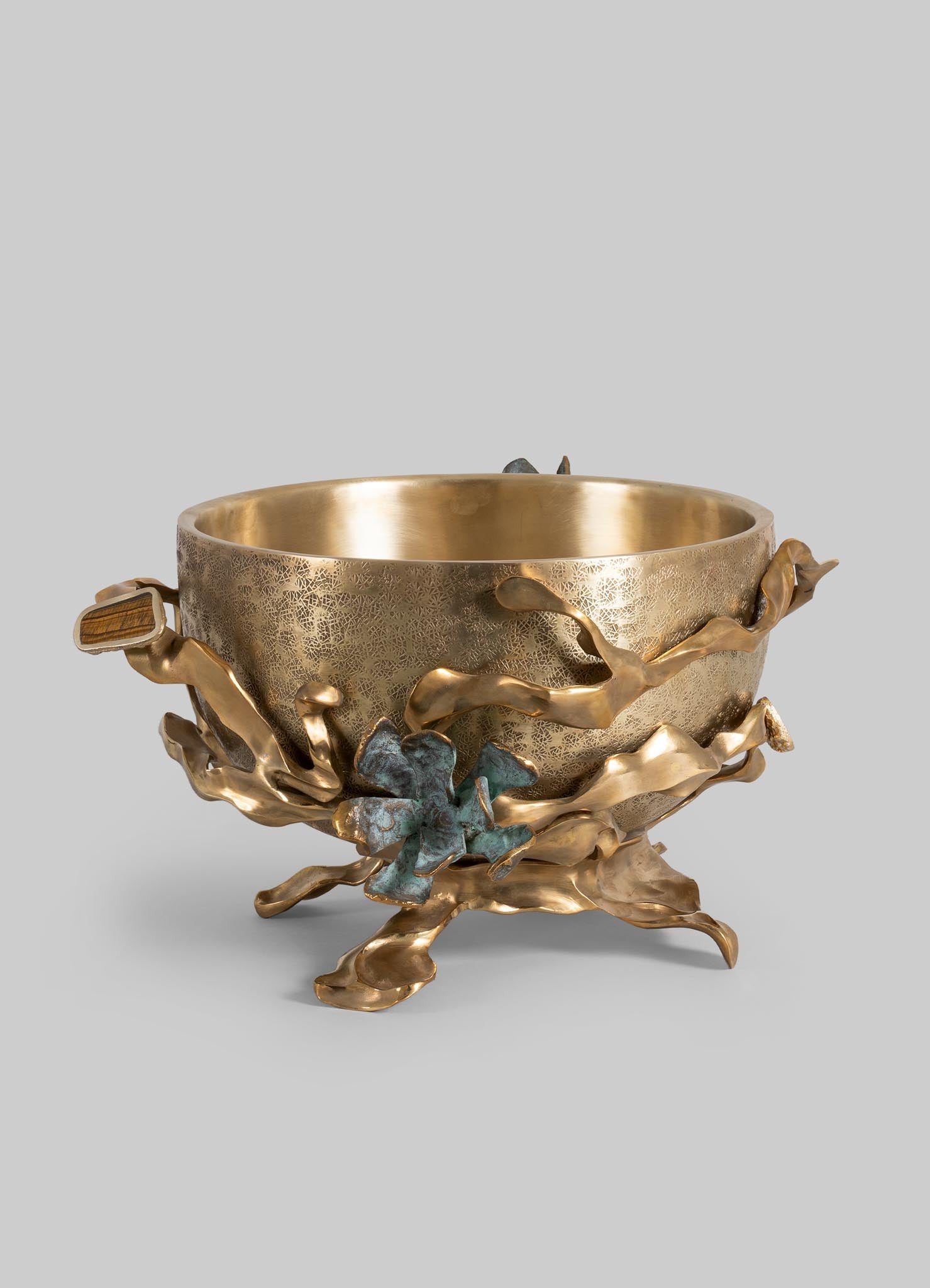 A decorative metal bowl with a textured gold interior and an organic, sculptural base featuring leafy and branch-like motifs in a mix of gold and patinated tones.