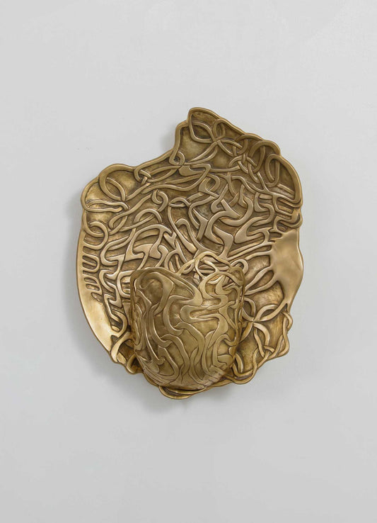 A decorative wall art piece crafted from metal with an intricate, organic design featuring swirling and looping motifs. The art has a metallic finish with warm gold tones, set against a plain, light-colored background.