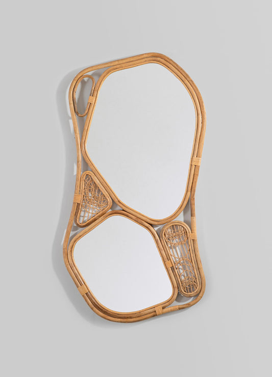 Woven rattan mirror with an irregular, organic shape featuring two mirror panels and decorative rattan motifs, mounted on a light grey wall.