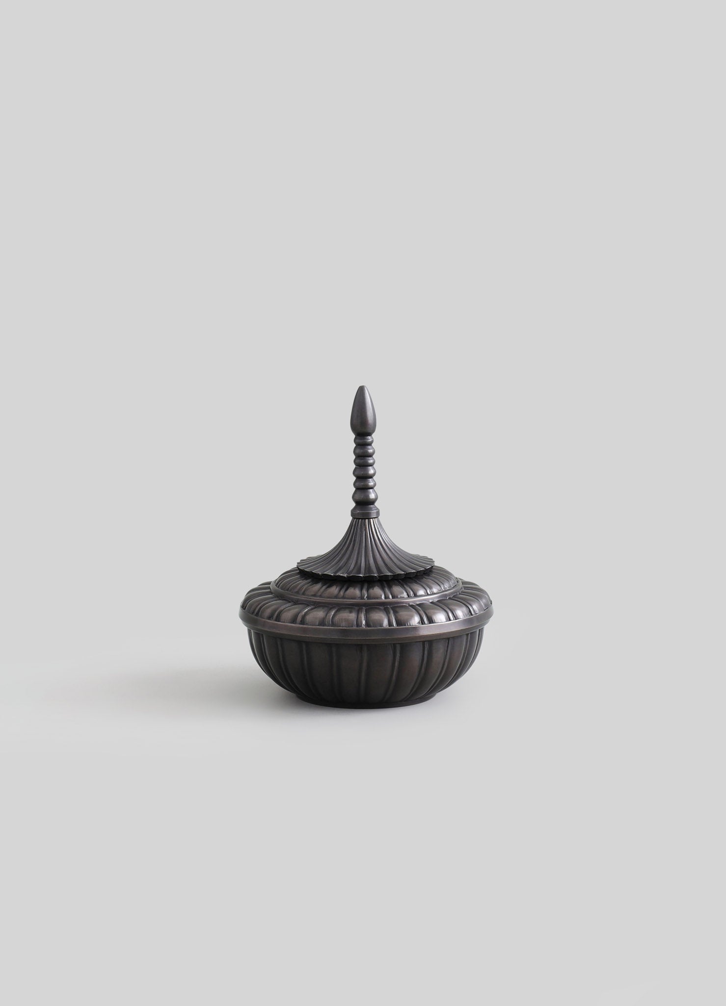 Decorative metal container with a dark, matte finish featuring a ribbed, rounded base and a fluted lid with a finial handle, inspired by traditional Asian design.