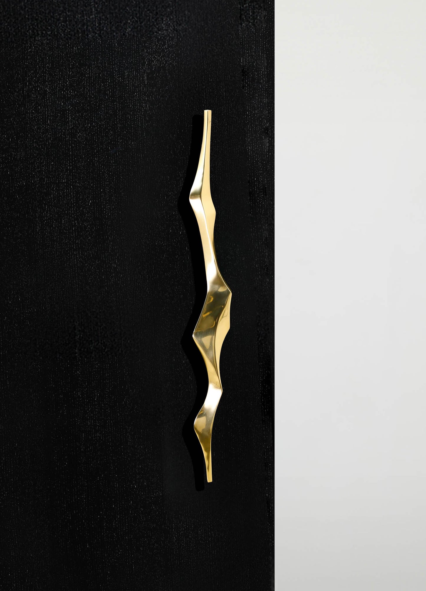 A decorative hand-shaped sculpture in polished gold metal with an abstract, modern design, displayed against a black textured surface and a neutral background.