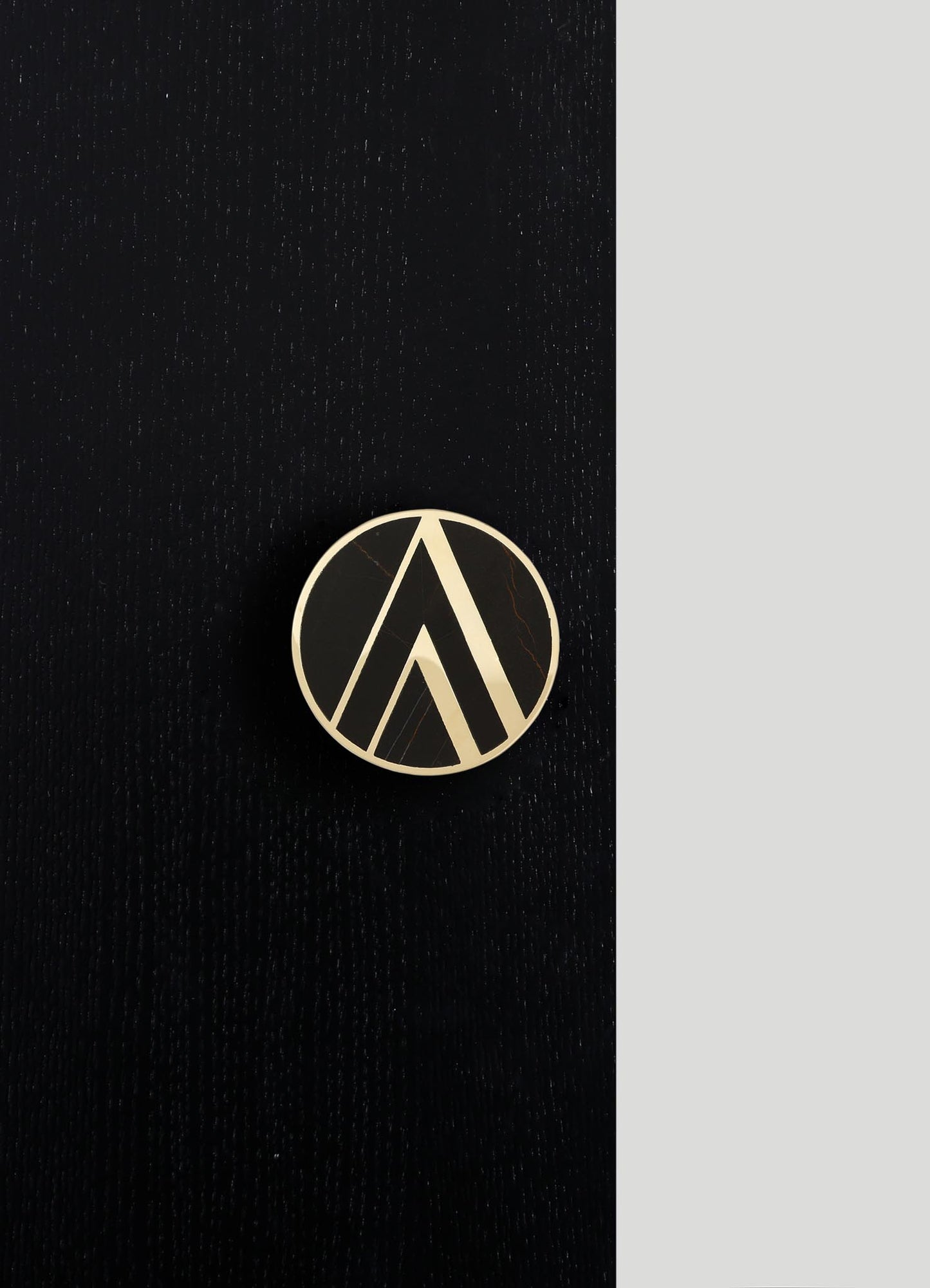 A round brooch with geometric black and beige patterns, featuring angular lines and a polished finish, placed on a textured black surface with a contrasting gray background.