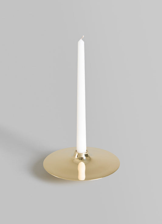 A minimalist brass candle holder with a round base and a tall, slender white candle. The holder has a polished finish and a contemporary design.