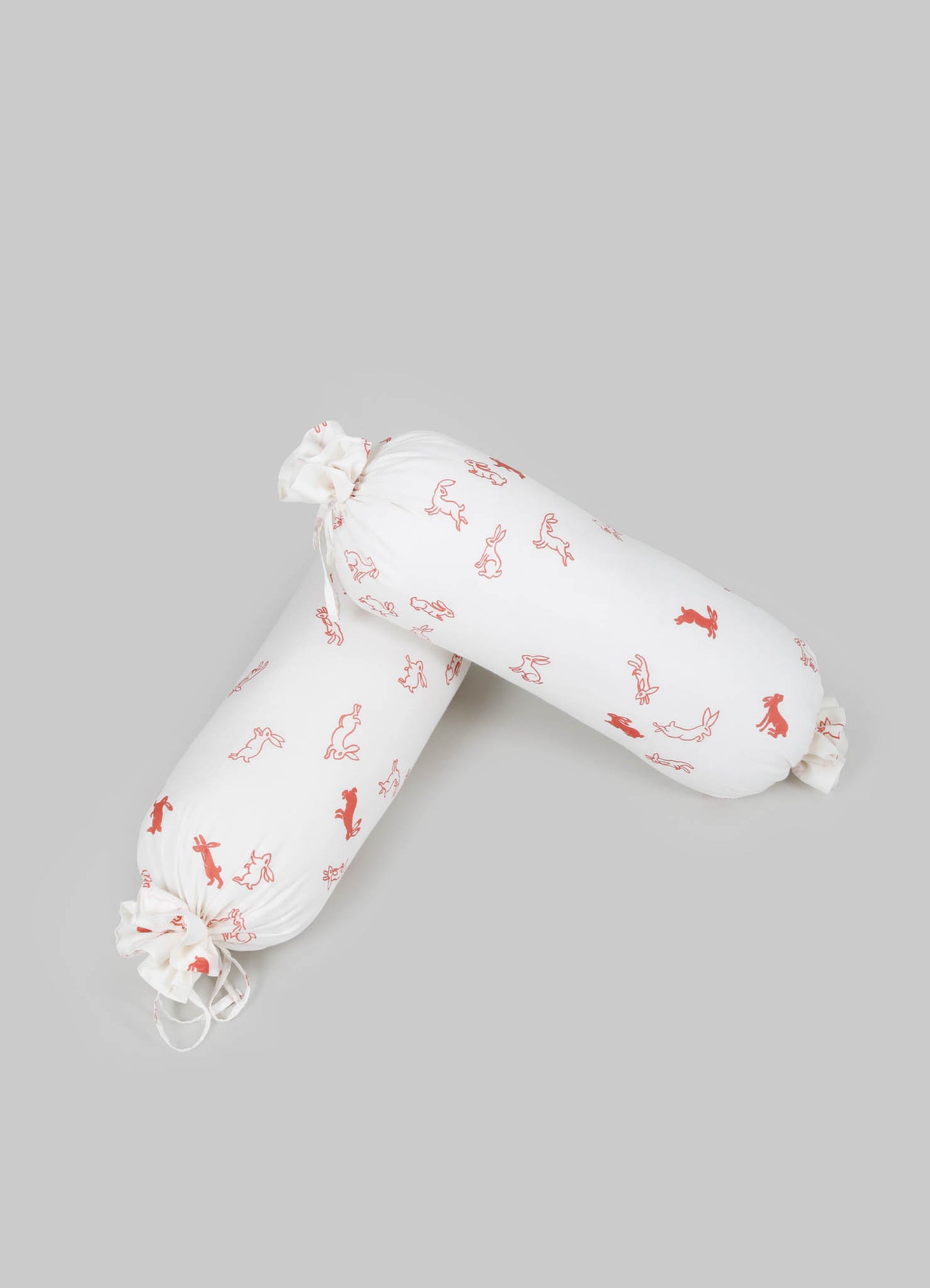 White fabric bolster cushions with a red animal and floral print, tied at each end with fabric ties, on a neutral background.