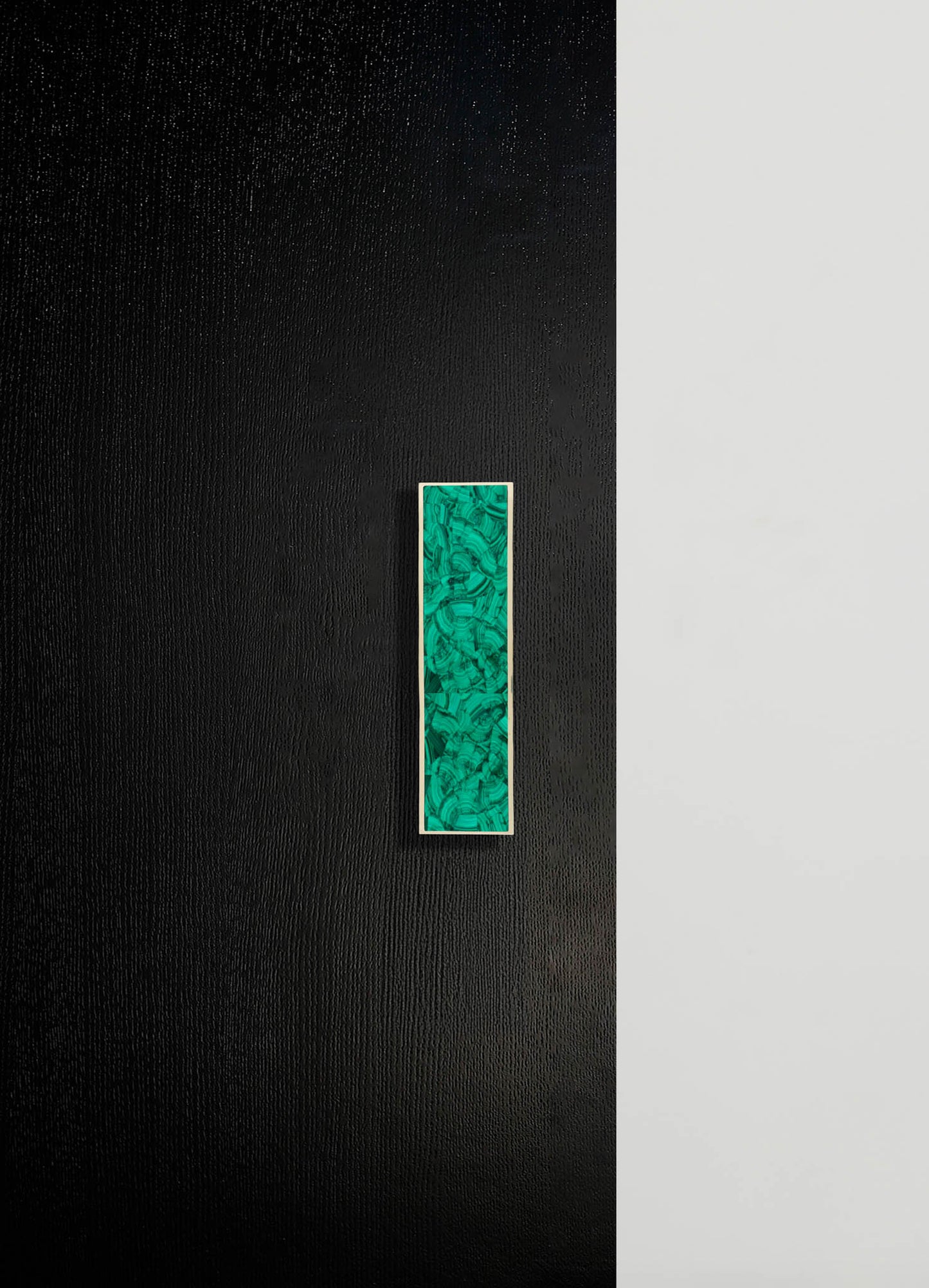 A black textured surface with a vertical rectangular inset of green malachite pattern bordered by a thin white frame.