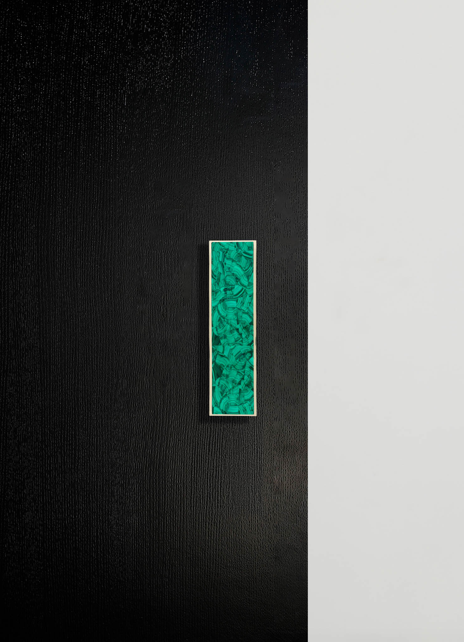 A black textured surface with a vertical rectangular inset of green malachite pattern bordered by a thin white frame.
