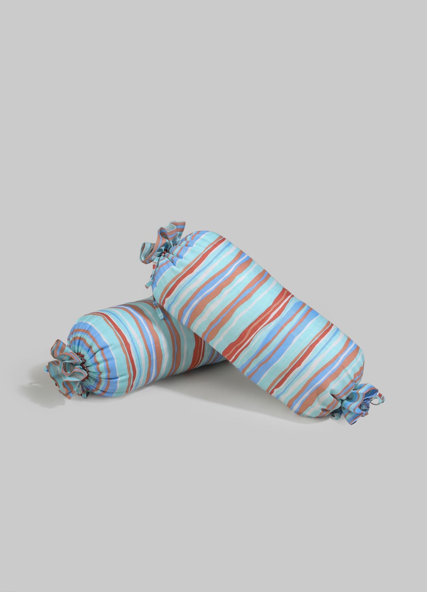 Striped fabric cushions with a multicolored pattern in blue, beige, and brown tones, tied at the ends with ruffled fabric.