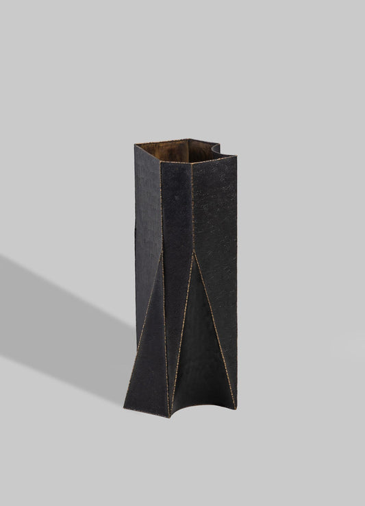 A tall, geometric vase made of black coated material with visible stitching lines and angular facets, featuring a gold interior.