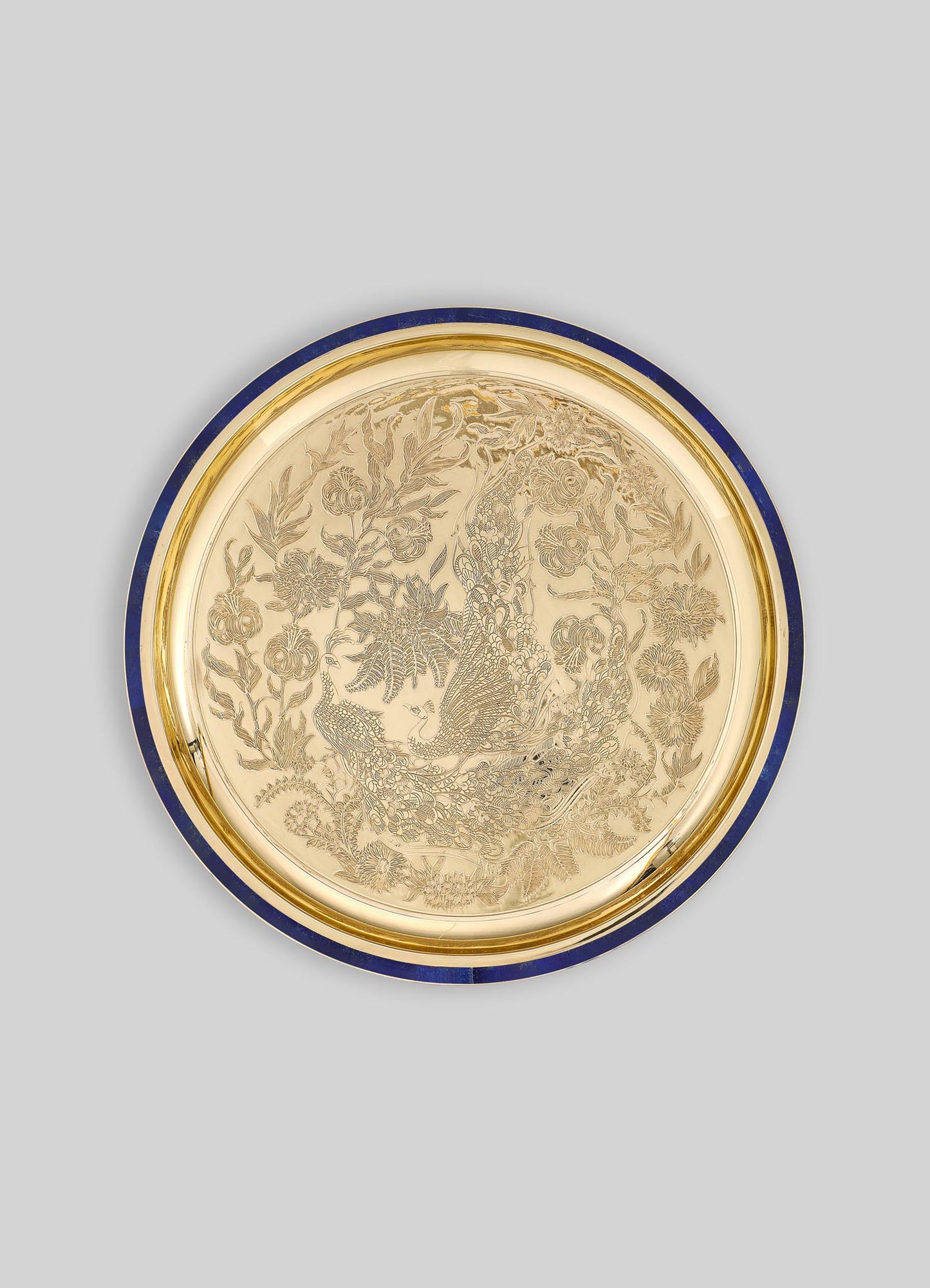A decorative round tray with a gold-toned surface and intricate engraved floral and peacock motifs. The tray features a dark blue border and appears to be made of metal or similarly polished material, with a luxurious and ornate style.