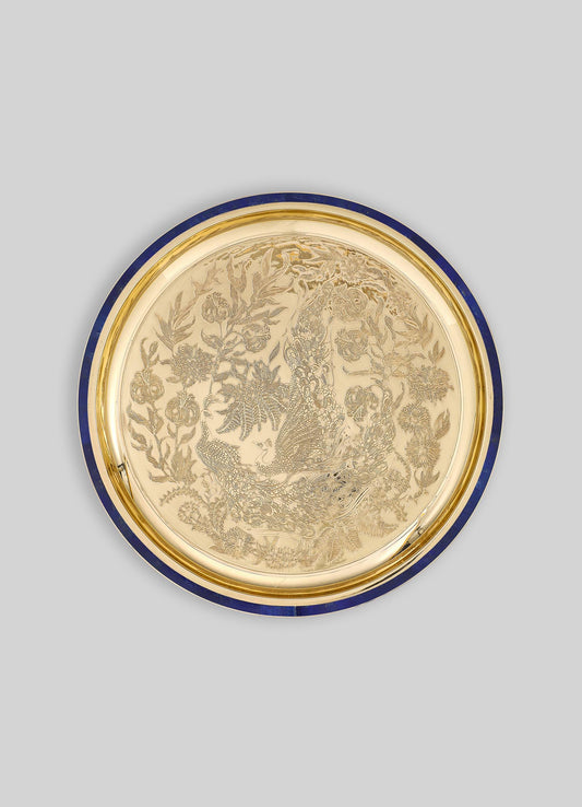 A decorative round tray with a gold-toned surface and intricate engraved floral and peacock motifs. The tray features a dark blue border and appears to be made of metal or similarly polished material, with a luxurious and ornate style.