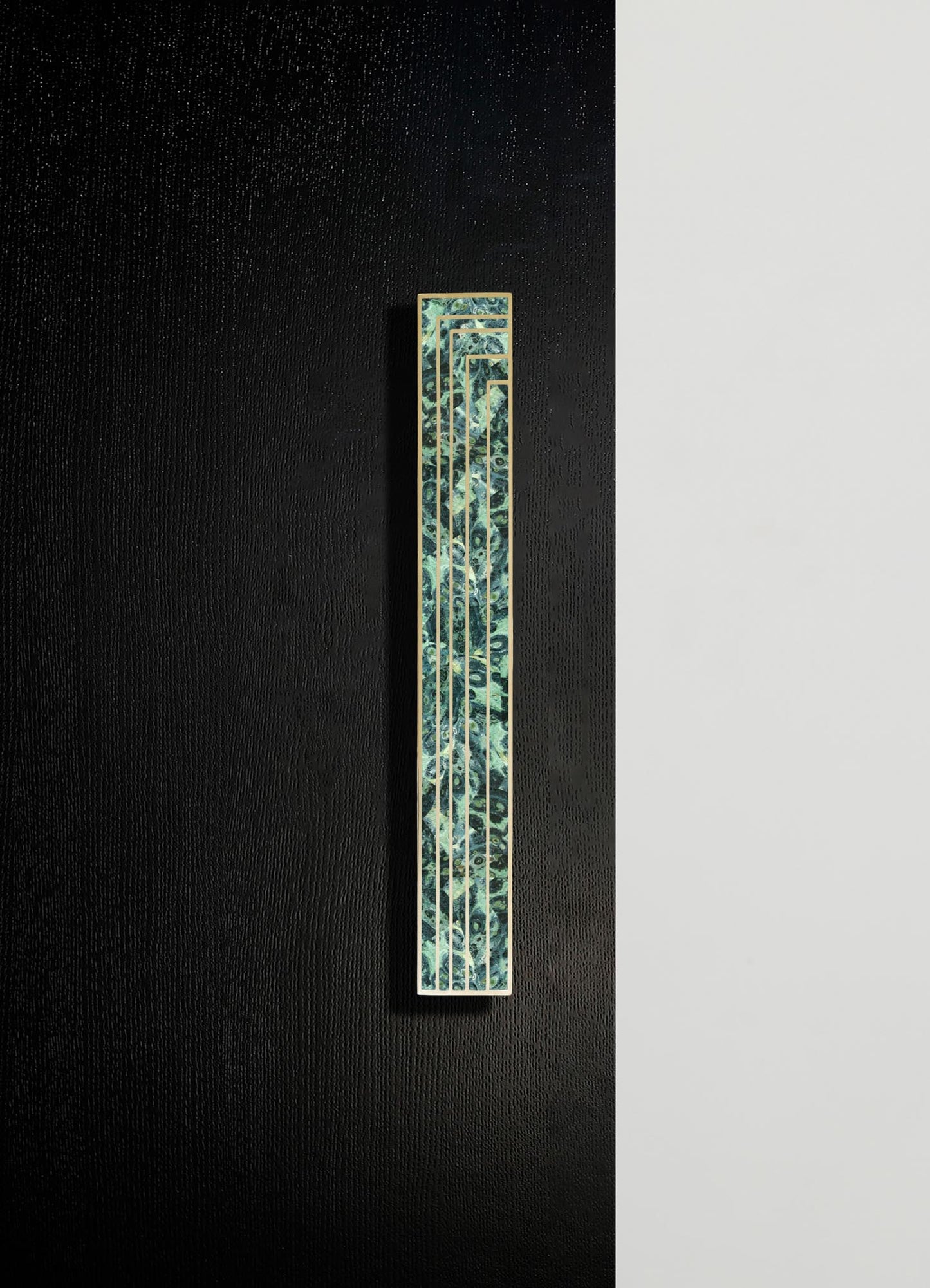 A decorative wall piece featuring a rectangular panel with a floral and marble-inspired motif in shades of green, blue, and white, bordered by a thin metallic frame. The panel is mounted on a textured black wall with a contrasting light grey section.