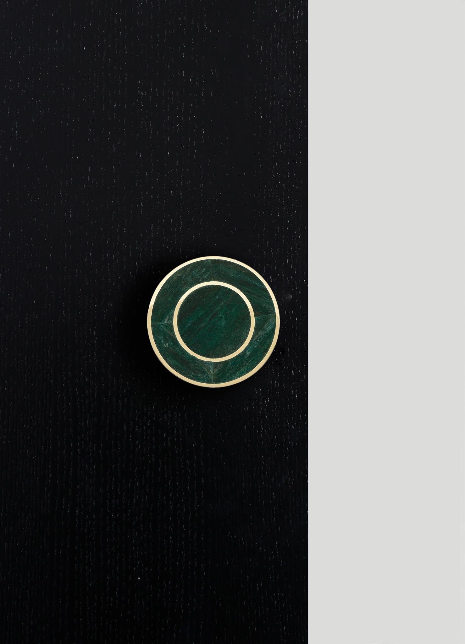 A round jewelry box with a dark green marble finish and a gold metal rim, placed on a black textured surface with a contrasting light gray background.