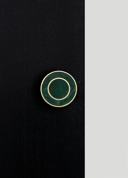 A round jewelry box with a dark green marble finish and a gold metal rim, placed on a black textured surface with a contrasting light gray background.
