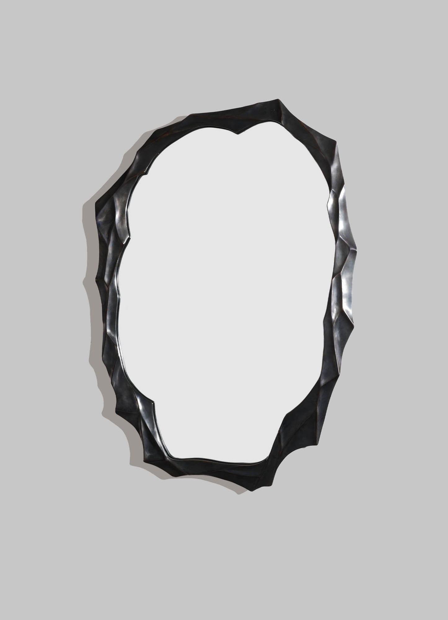 A decorative wall mirror with a textured, irregular black frame and an oval reflective surface.