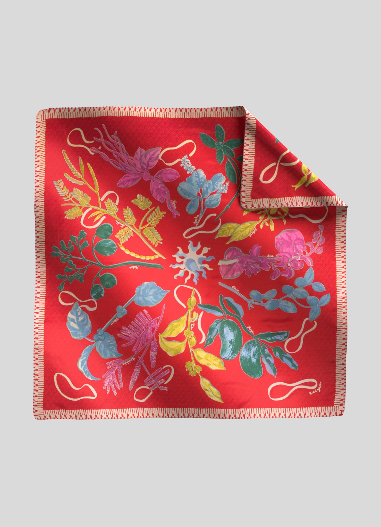 A silk scarf with a vibrant red background features a floral motif in shades of pink, purple, blue, and green, accented with white and yellow details. The edges are finished with a decorative stitched border.