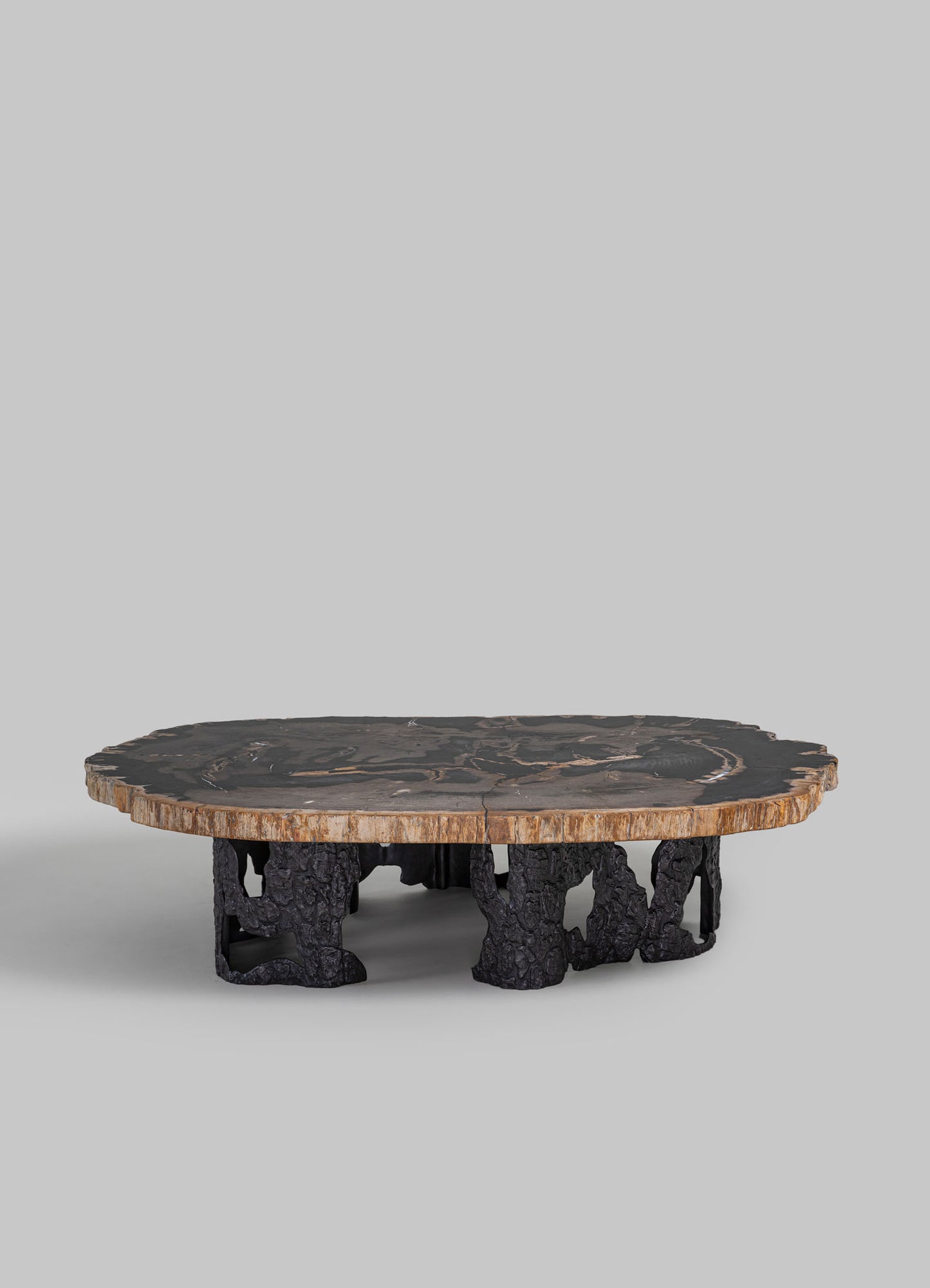 A low coffee table with a thick, round wooden top featuring natural edge details and a dark, polished finish, supported by sculptural black metal legs with an organic, textured appearance.