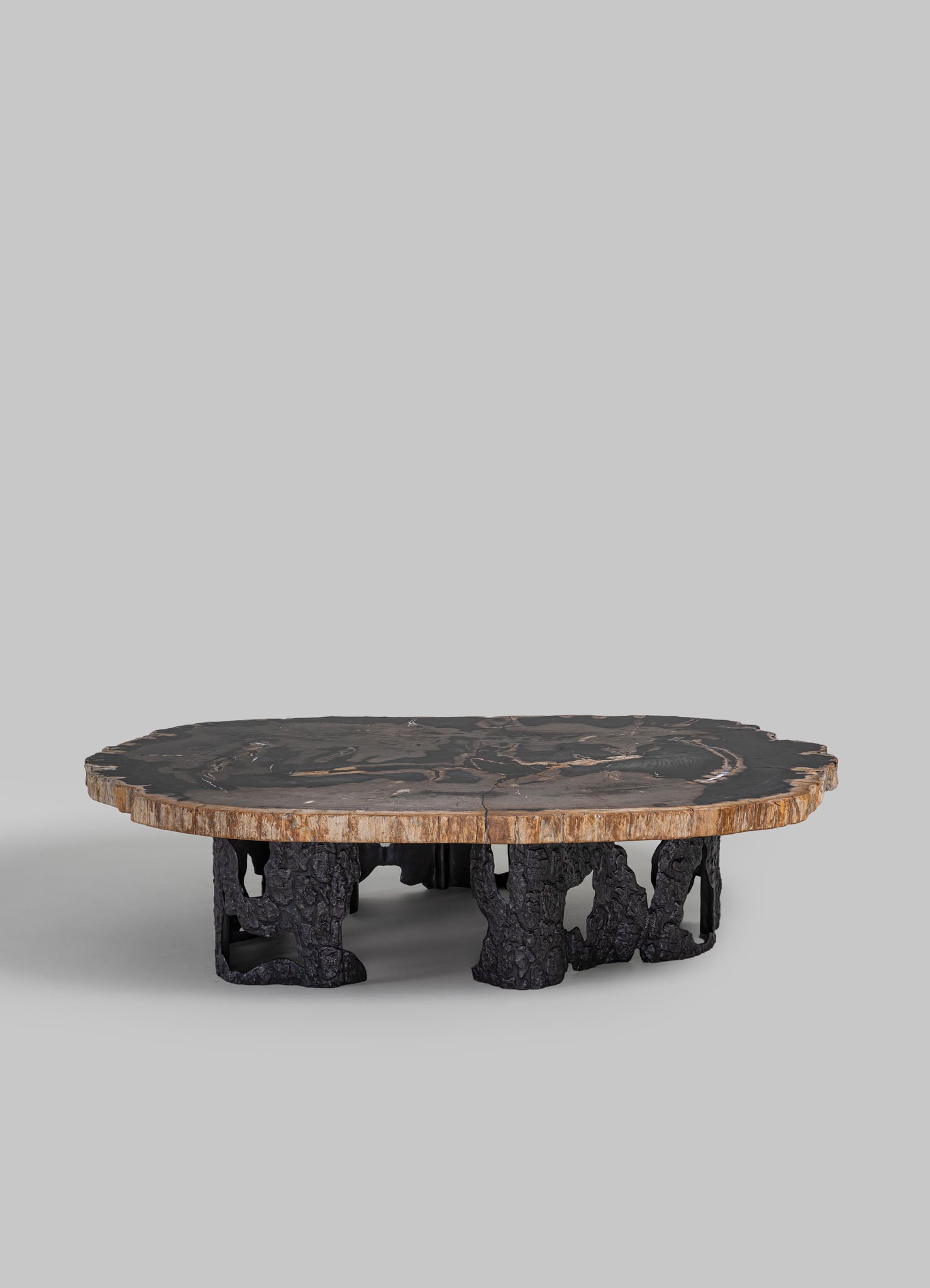 A low coffee table with a thick, round wooden top featuring natural edge details and a dark, polished finish, supported by sculptural black metal legs with an organic, textured appearance.