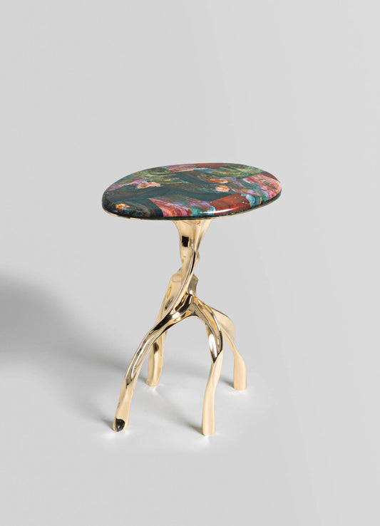 A side table with a round, multicolored stone top featuring abstract patterns and a glossy finish, supported by a sculptural, polished gold-metallic base with irregular, organic forms.