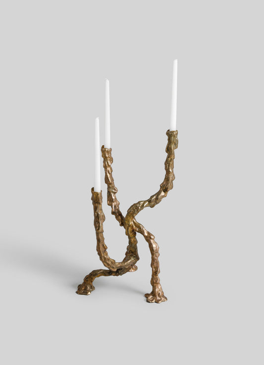 Brass candelabra with a sculptural, organic design resembling intertwined branches, featuring three white tapered candles.