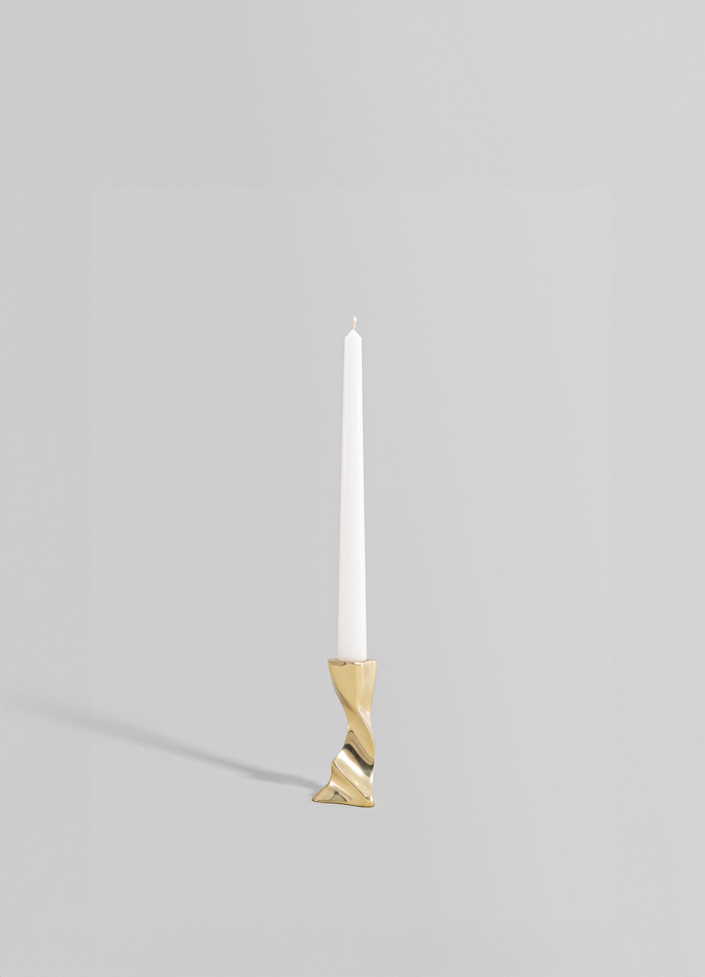 A tall, slender candle holder made of metal with a gold finish, featuring an abstract, twisted design at the base, holding a white taper candle.