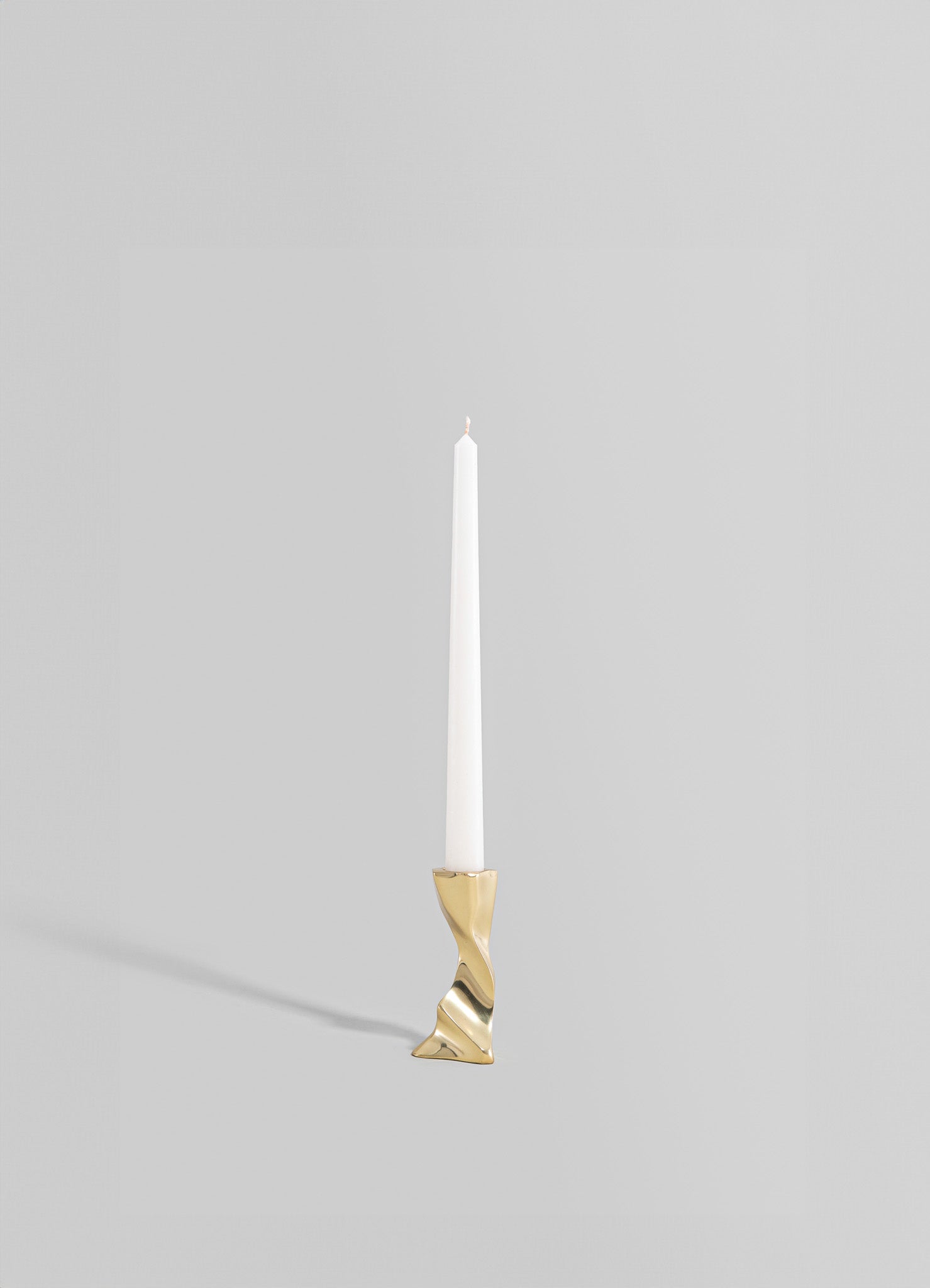 A tall, slender candle holder made of metal with a gold finish, featuring an abstract, twisted design at the base, holding a white taper candle.
