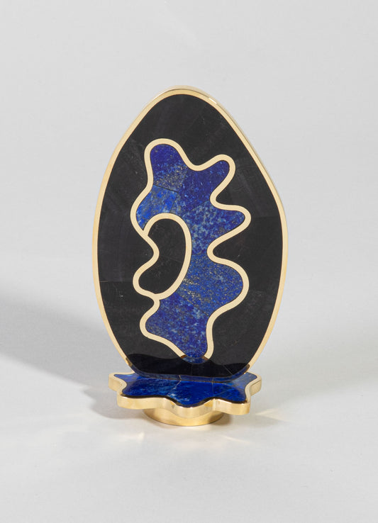 Decorative sculpture with an abstract organic shape featuring blue and gold speckled inlay, set against black stone with gold trim accents. The sculpture stands on a matching blue and gold base, crafted in a contemporary style.