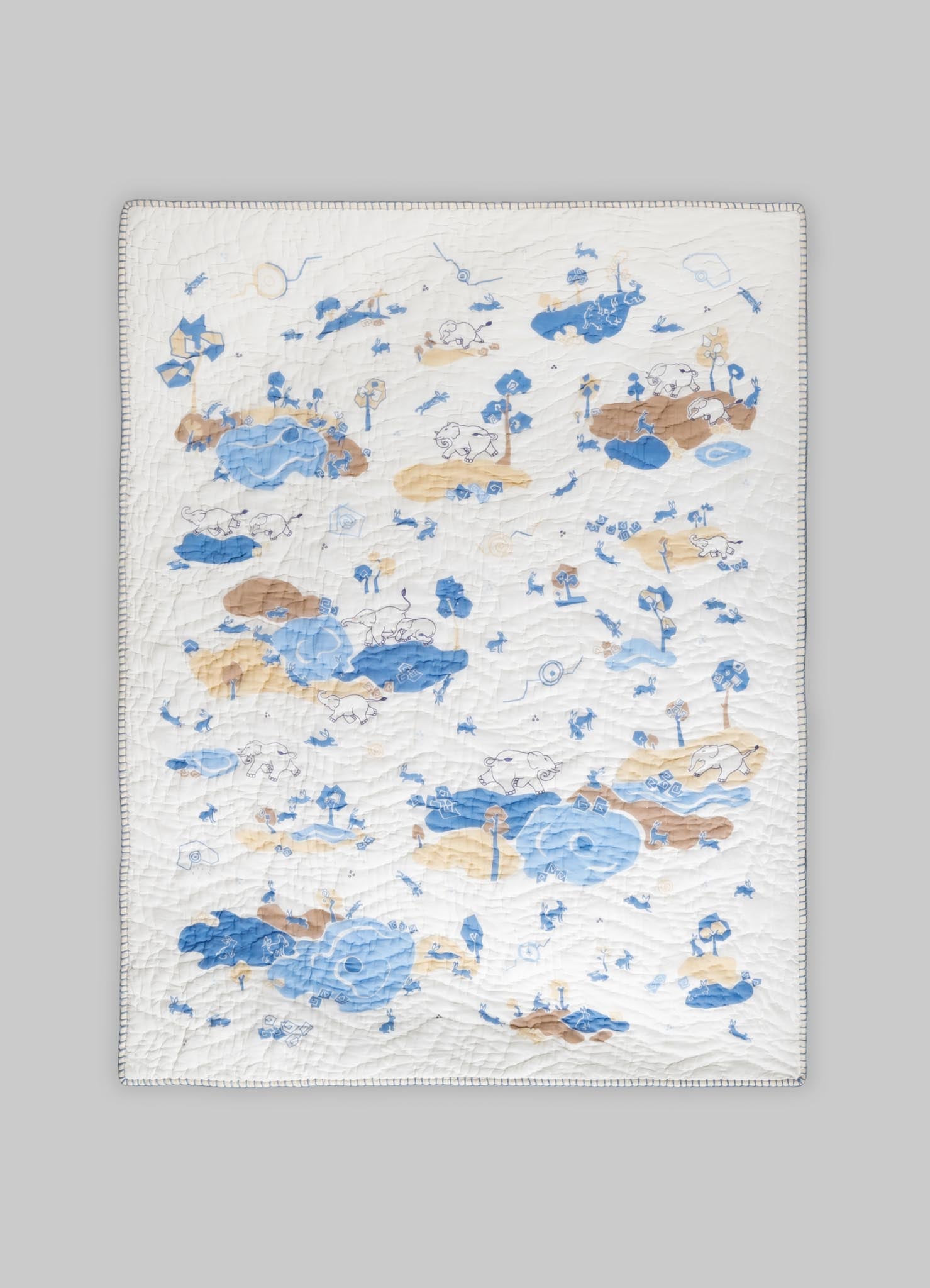 Quilt with a whimsical animal and nature motif in shades of blue and beige on a white background, featuring stitched details and a repeating pattern.