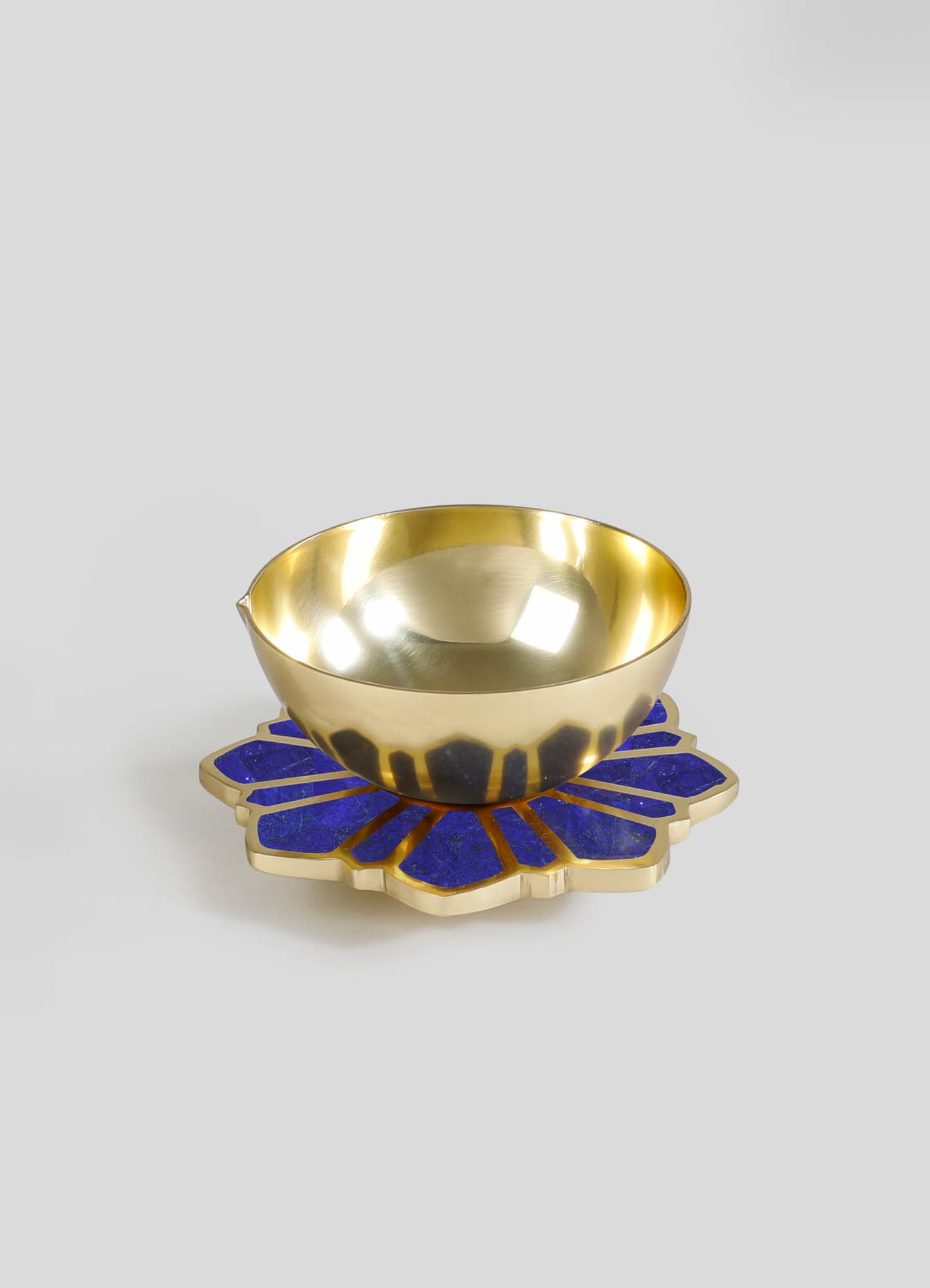 A gold-colored metal bowl with a polished finish, placed on a decorative blue and gold flower-shaped coaster or tray.