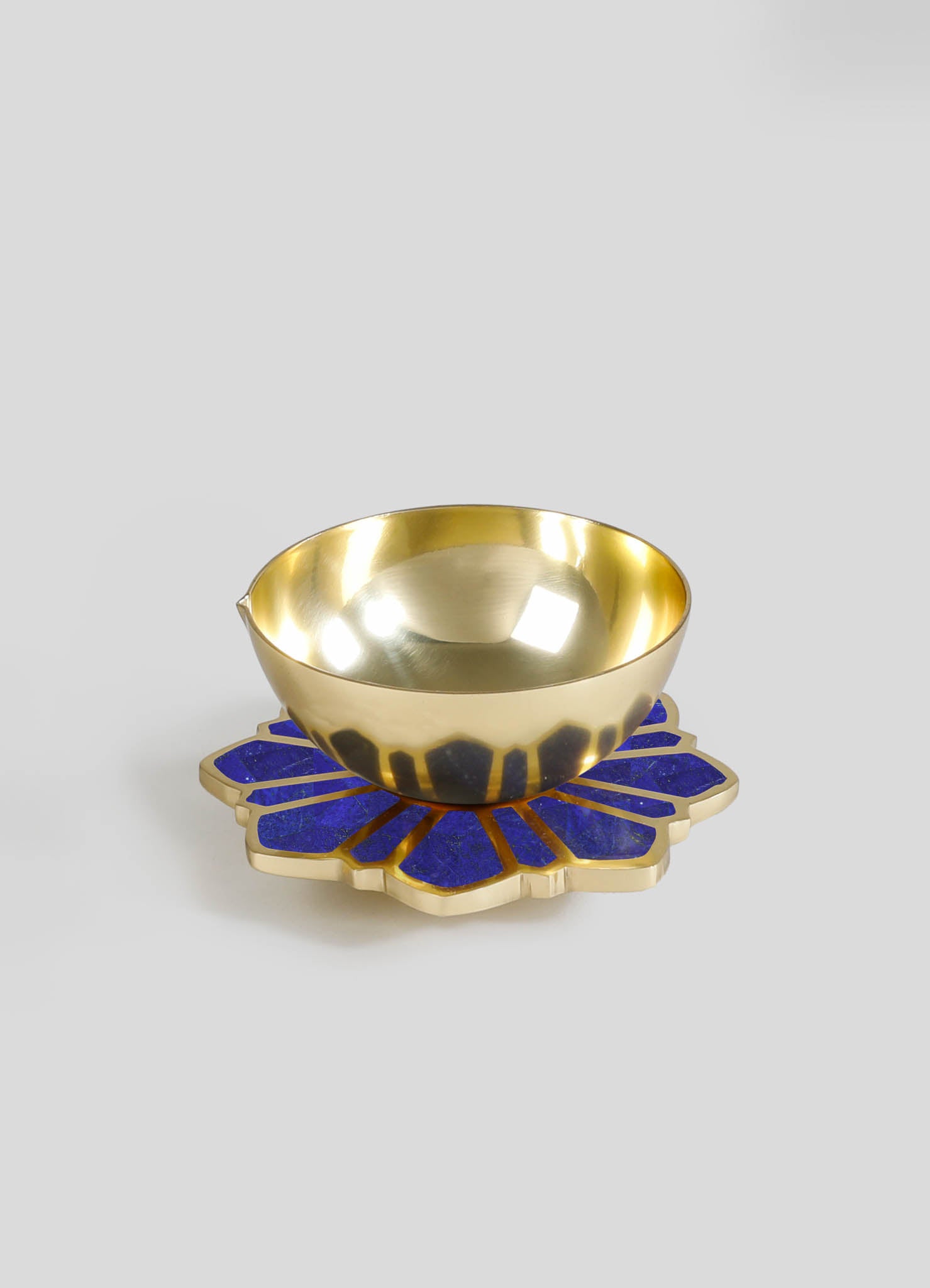 A gold-colored metal bowl with a polished finish, placed on a decorative blue and gold flower-shaped coaster or tray.