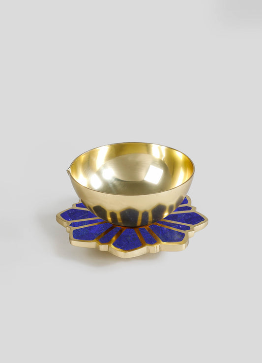 A gold-colored metal bowl with a polished finish, placed on a decorative blue and gold flower-shaped coaster or tray.