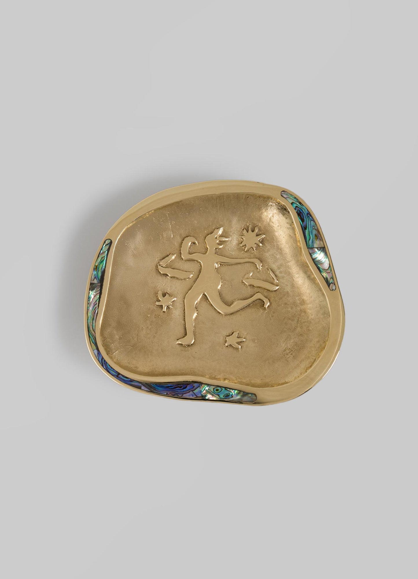 A decorative gold pocket mirror with an engraved figure and star motifs on the surface, featuring an colorful abalone shell inlay along the edge.
