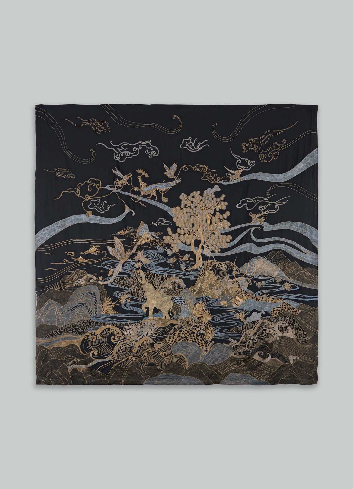 The Viya Dreamscape Black & Gold Embroidered Bedcover features intricate animal, bird, mountain, cloud, and tree motifs in gold and silver thread on black, showcasing the vibrant artistry of embroidered textiles.