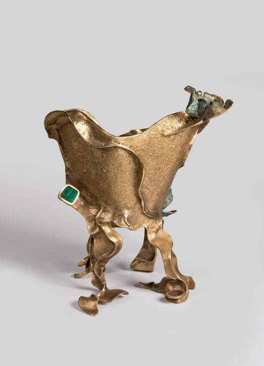 A sculptural decorative object made of textured brass with organic, flowing shapes and irregular, curling legs. It features accents of turquoise and green stones, with a prominent rectangular green gemstone set into one side.