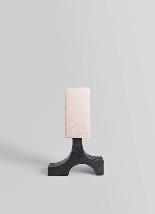 A table lamp with a black textured base featuring an arched design and a rectangular fabric shade in a soft beige tone, set against a plain light gray background.