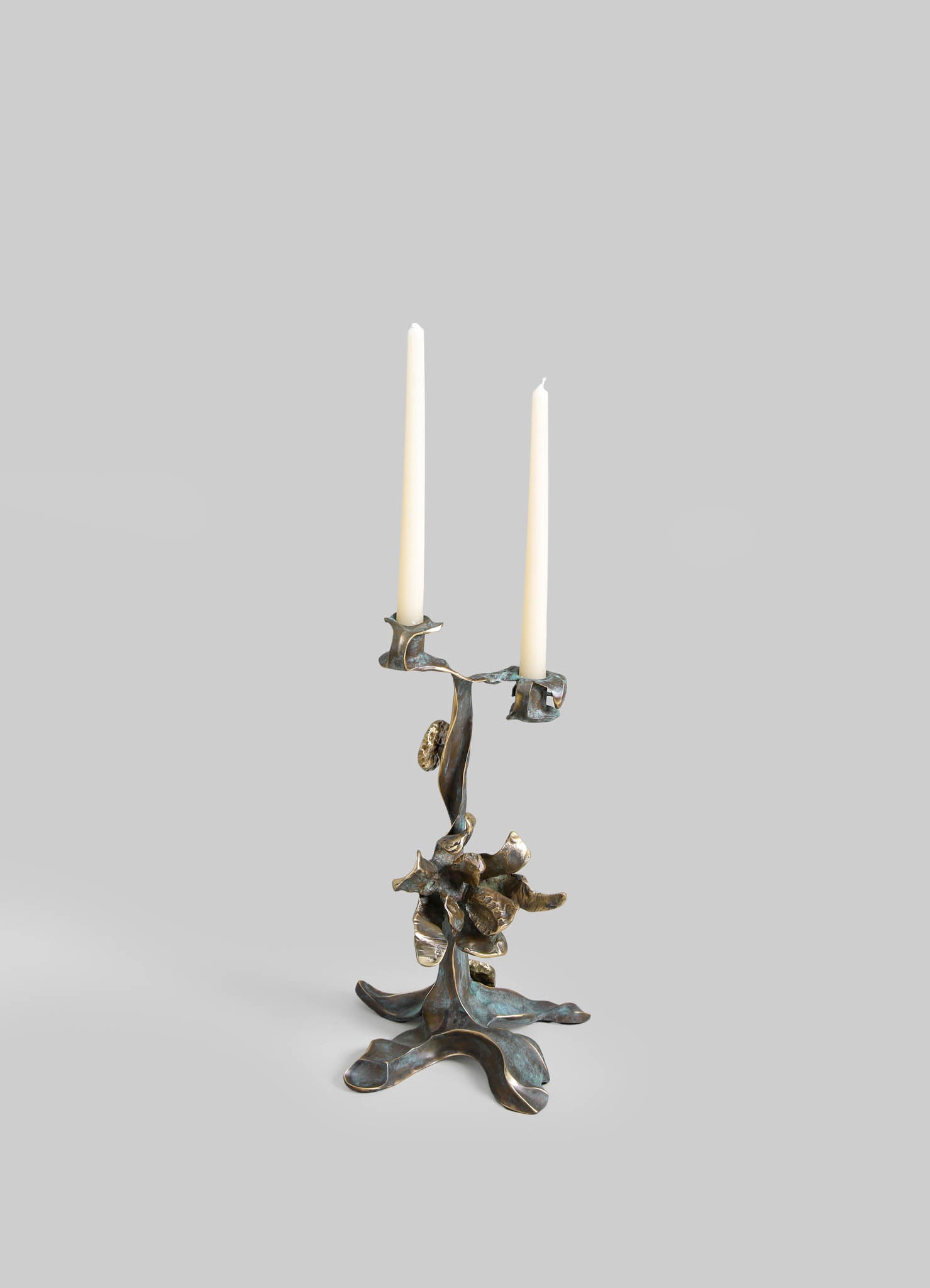 Metal candlestick holder with an abstract, organic design in brass with a tarnished finish, holding two white taper candles.
