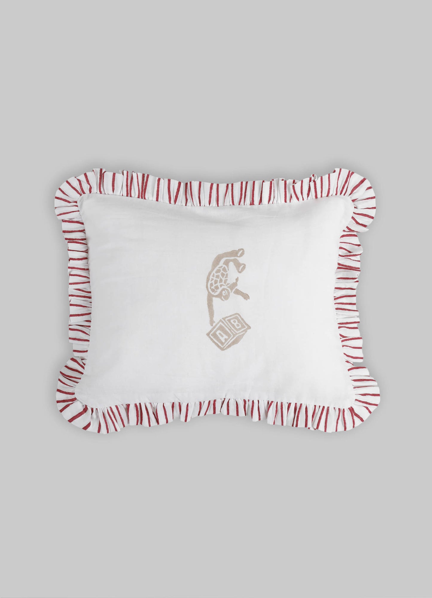Baby pillow with white fabric and embroidered animal motif in neutral tones, featuring a ruffled border with red and white striped pattern.