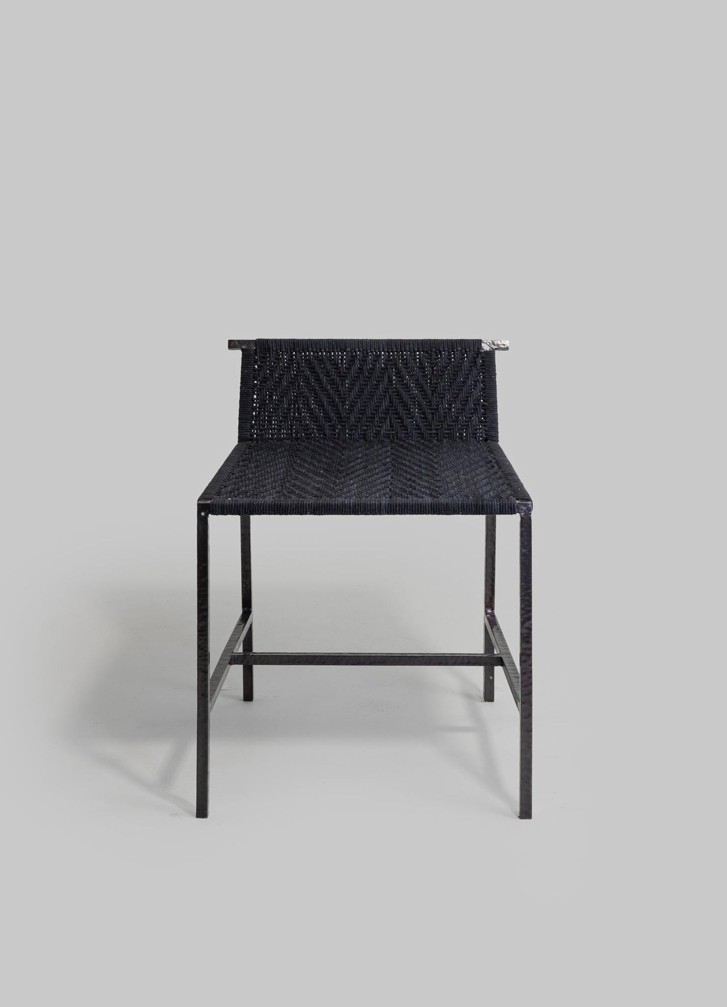 A black woven chair with a metal frame and a textured pattern on the seat and backrest, set against a light gray background. The design is minimalist and modern.