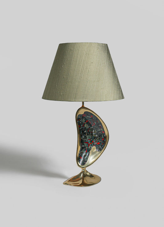 A table lamp with a ceramic base featuring an abstract, organic shape and a mosaic pattern in dark and red tones, topped with a neutral fabric lampshade.