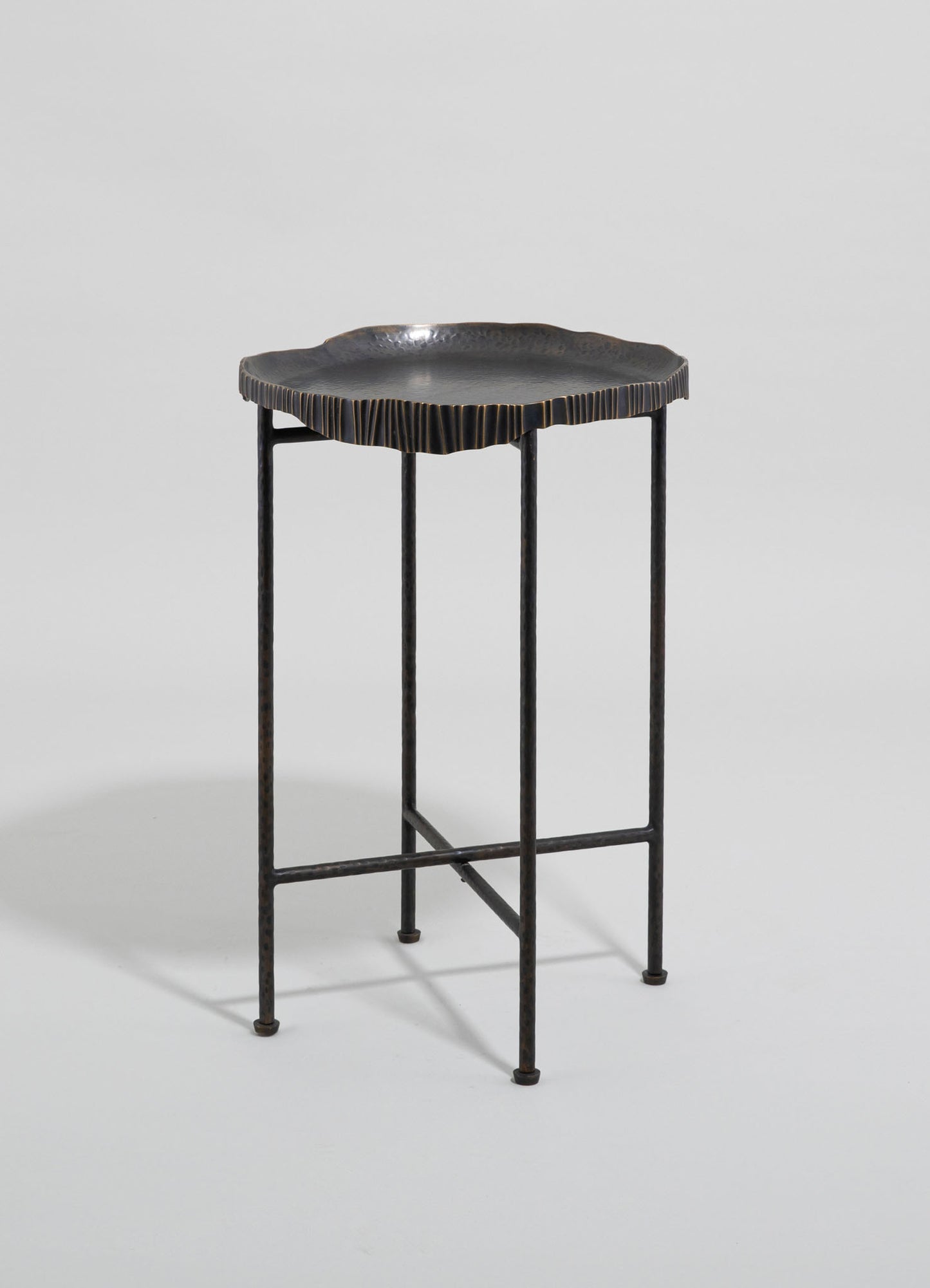 A small side table with a textured, irregularly shaped black top featuring a metallic finish and a slightly rippled edge, supported by a slender, black metal frame with four straight legs.