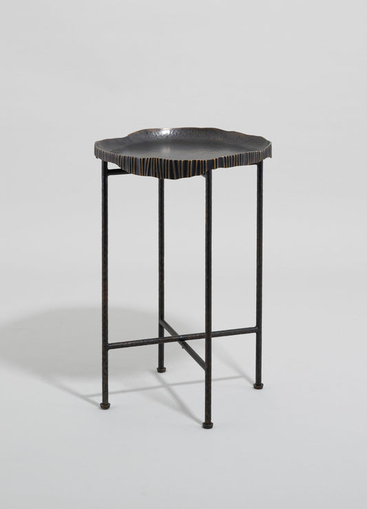 A small side table with a textured, irregularly shaped black top featuring a metallic finish and a slightly rippled edge, supported by a slender, black metal frame with four straight legs.