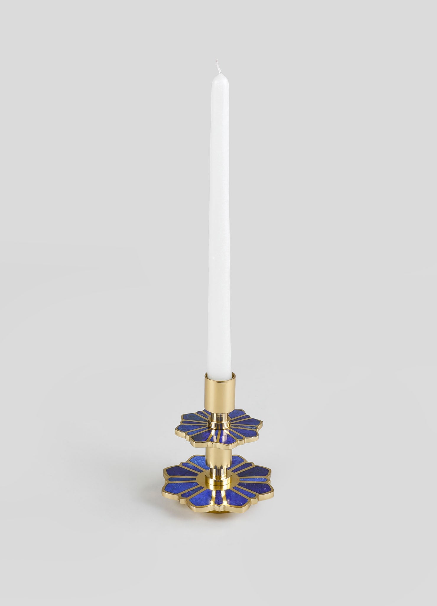A brass candle holder with blue enamel floral motifs and a gold finish, designed to hold a tall white taper candle.