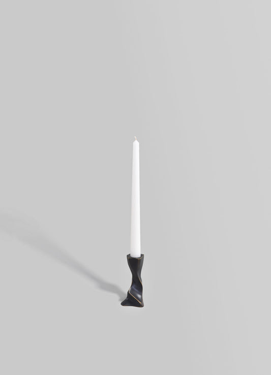 A candlestick holder with a sculptural, twisted design in matte black finish, holding a tall white pillar candle.