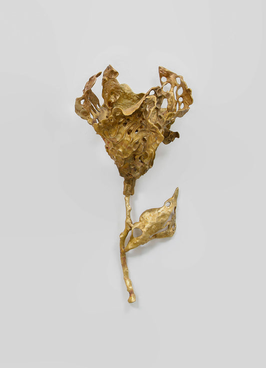 A sculptural wall decor piece made of metallic gold-toned material with an abstract, organic form featuring irregular, perforated surfaces and flowing, ruffled textures.