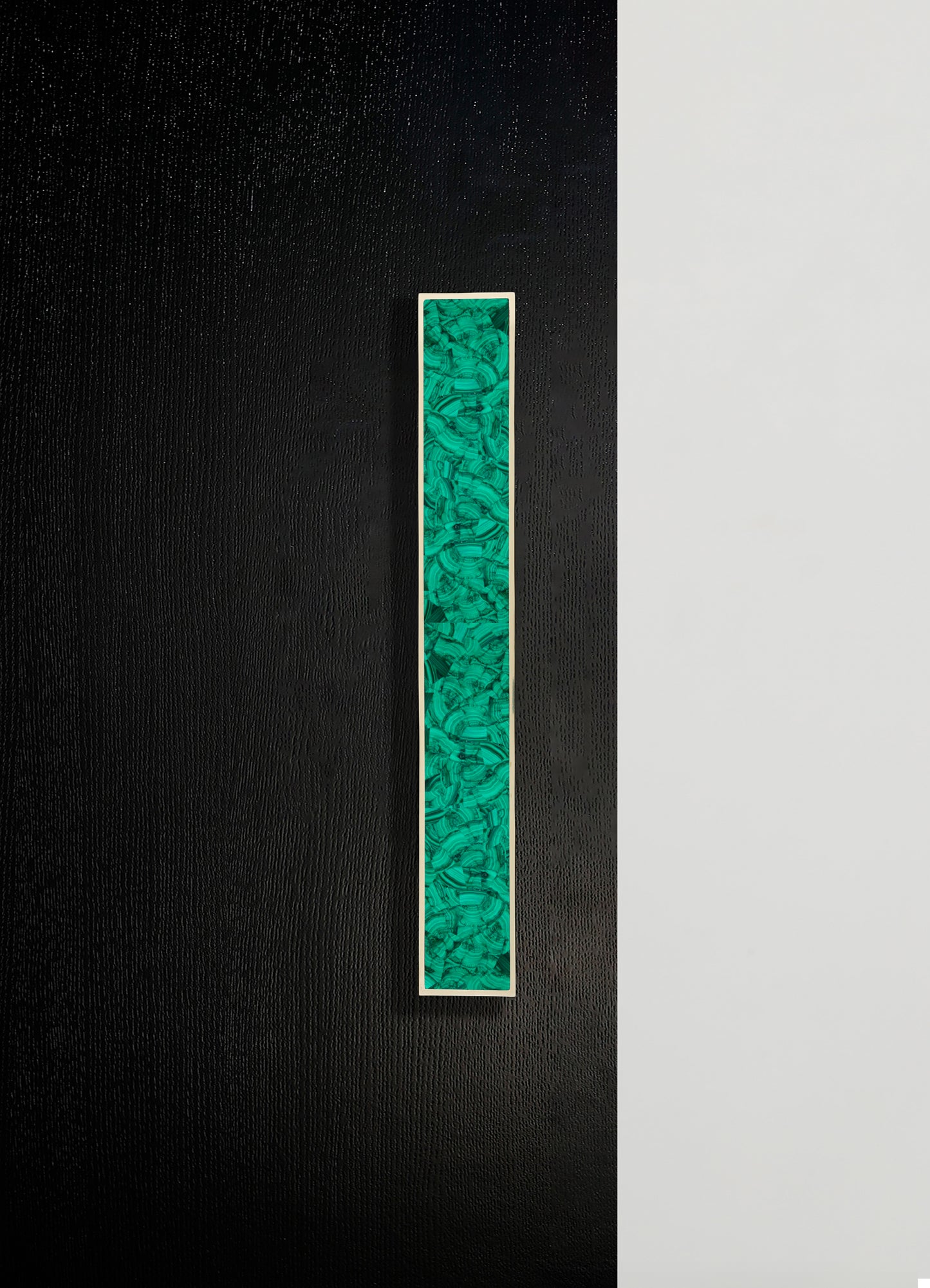 A long rectangular artwork with an abstract pattern in shades of green and black, framed with a thin white border, mounted on a textured black wall.