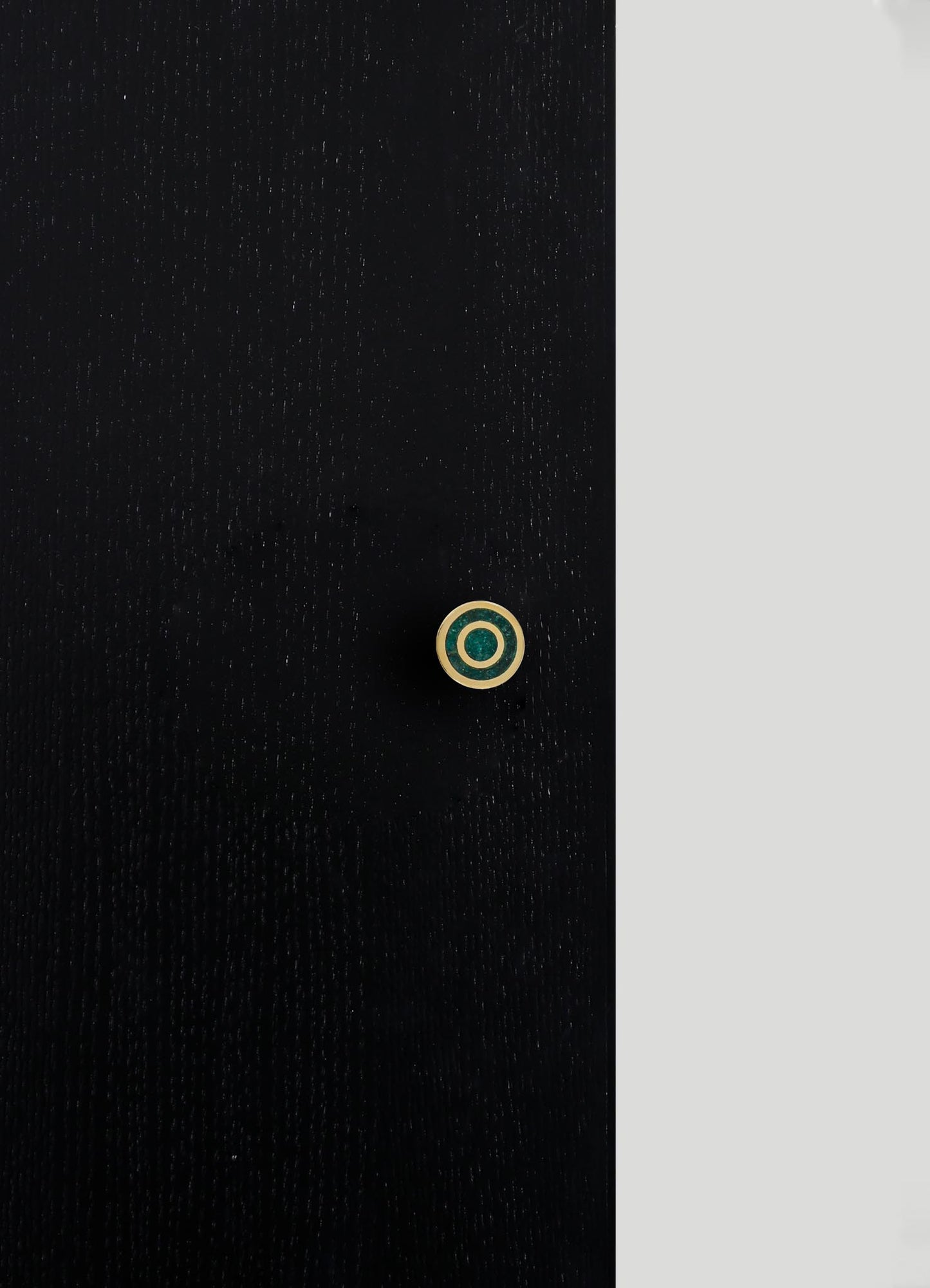 A close-up of a black fabric garment with a small circular button featuring a gold and dark green concentric design. The fabric has a subtle sheen and a fine textured weave.