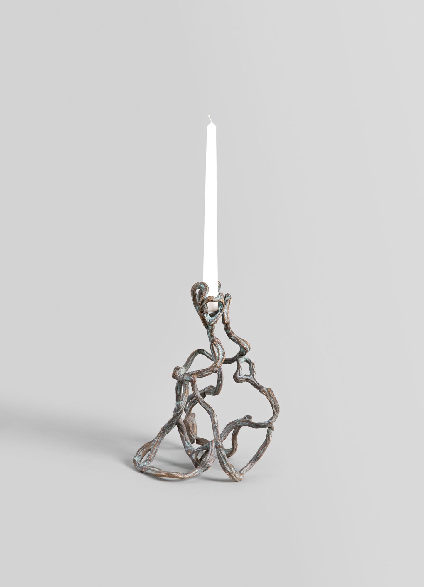 A metallic candle holder with an organic, twisted design resembling intertwined branches, holding a tall white taper candle against a neutral background.